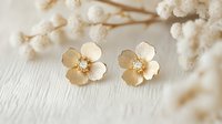 Delicate gold flower stud earrings with crystal centers on light background with baby's breath flowers, feminine jewelry photography for fashion blog.