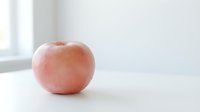 Fresh pink apple on white surface with natural light, suitable for healthy eating, nutrition, and food photography projects.