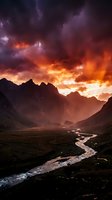 Dramatic mountain landscape with winding river at sunset, fiery orange and purple storm clouds illuminating rugged peaks and valley terrain for nature, travel, and environmental design projects.