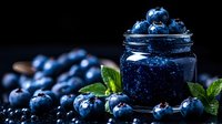 Fresh ripe blueberries and homemade jam in glass jar on dark background with mint leaves, moody food photography for healthy eating and preserves.