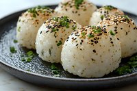 Japanese rice balls onigiri with sesame seeds and fresh herbs served on dark ceramic plate, traditional Asian cuisine close up macro food photography.