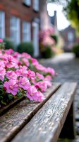 Vibrant pink flowers bloom beside weathered wooden bench on cobblestone path, with brick houses creating charming residential backdrop.