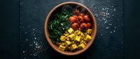 Colorful roasted vegetables in terracotta bowl on dark slate surface with sea salt scattered around, overhead view for food styling, cooking, nutrition, and recipe content.