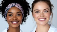 Young African American and Caucasian women with bright genuine smiles wearing white tops against light background, representing diversity, friendship and healthcare.