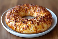 Golden braided bread ring with glossy crust on white plate, freshly baked pastry with rich brown color perfect for breakfast or holiday dining table.