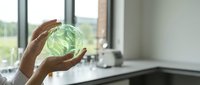 Fresh green cabbage head held in hands over modern kitchen counter with natural window lighting for healthy cooking and meal preparation.