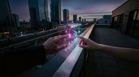 Hand holding glowing digital hologram over urban cityscape at sunset with futuristic technology interface and modern skyscrapers in background.