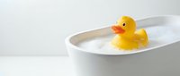 Yellow rubber duck floating in white bathtub with water, classic bath toy for children's playtime and bathroom decor in clean modern setting.