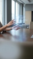 Woman's hands holding holographic digital data visualization with flowing network lines and particles at wooden desk in modern office with bright windows.