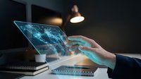 Close-up of hands holding transparent laptop with glowing blue digital network interface, representing technology, innovation, and digital transformation in modern workplace environment.