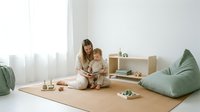 Young mother reading book with toddler in minimalist playroom with natural light and modern furniture for family bonding and early education.