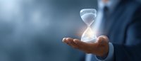 Businessman in suit holding glowing hourglass floating above palm against blue background, representing time management and business deadlines.