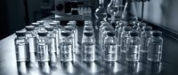 Medical vials and glass containers arranged on laboratory table for pharmaceutical research and drug development in sterile clinical environment.