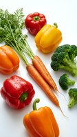 Fresh colorful vegetables including bell peppers, carrots, and broccoli with water drops on white background, for healthy food and nutrition content.