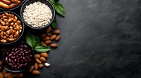 Healthy protein sources with legumes, nuts and grains in black bowls on dark stone background with fresh basil leaves and copy space for text.