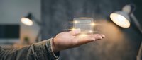 Businessman holding glowing holographic house symbol in palm, representing real estate technology, smart home innovation, and digital property investment solutions.