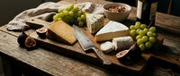 Artisanal cheese board with aged cheddar, blue cheese, fresh grapes, nuts and bread on wooden serving platter for entertaining and food styling.