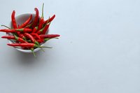 Fresh red chili peppers in white ceramic bowl on light gray background, minimalist food photography with copy space.