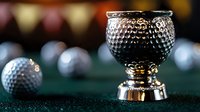 Elegant silver trophy cup with golf ball texture on dark green surface, dramatic lighting creates luxurious atmosphere. Additional golf balls in soft focus background.