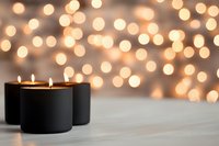 Lit black candles on white wooden surface with warm golden bokeh lights in soft focus background, suitable for holiday, wellness, and home decor designs.