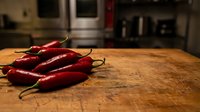 Fresh red chili peppers on wooden cutting board in modern kitchen ready for cooking spicy dishes and culinary preparations.