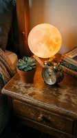 Cozy bedroom nightstand with glowing moon lamp, succulent plant, vintage alarm clock and books creating warm ambient lighting for relaxation and sleep.