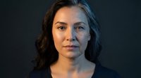 Professional portrait of confident middle-aged Caucasian businesswoman with brown wavy hair against dark background for corporate marketing materials.