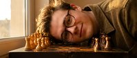 Young woman with glasses resting head on wooden table with golden honeycomb in warm sunlight streaming through window creating cozy morning atmosphere.