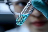 Laboratory test tube with sparkling blue liquid and bubbles held by scientist in protective gloves during chemical research experiment in medical lab.