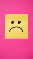 Yellow sticky note with sad face emoticon on bright pink background expressing disappointment and negative emotions for mental health concepts.
