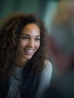 Young woman with curly hair smiling warmly against blurred background, conveying happiness and confidence in casual setting.