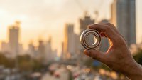 Hand holding lens focusing on urban skyline at sunset, symbolizing vision, perspective, and photography focus for creative professionals.