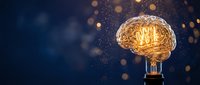 Glowing brain-shaped light bulb with golden filaments against dark blue background with bokeh lights representing creativity and innovation concepts.