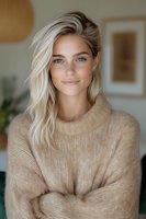 Young Caucasian woman with blonde hair wearing beige knit sweater smiling at camera. Natural makeup, bright eyes, and soft lighting create warm, friendly atmosphere for lifestyle and beauty content.