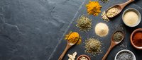 Assorted dried spices and herbs arranged with wooden spoons on dark slate surface for cooking, seasoning, and culinary design projects.