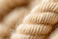 Soft beige natural cotton rope in macro view showing detailed twisted fiber texture and patterns. Suitable for craft and nautical design backgrounds.