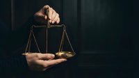 Professional lawyer holding golden scales of justice in dark courtroom setting representing legal services and judicial system.