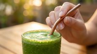 Young adult hand holding reusable metal straw in fresh green smoothie drink outdoors, sustainable lifestyle and eco-friendly beverage consumption concept.