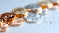 Shiny gold and silver coins scattered on light surface with water droplets, creating luxurious financial concept with selective focus and bokeh effect.