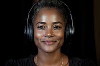 Young African American woman wearing black headphones smiling at camera against dark background for music and audio content.