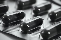 Black and white macro shot of medical capsules in blister pack, showing transparent gelatin capsules filled with dark powder, pharmaceutical industry concept.