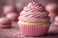 Pink frosted vanilla cupcake with sprinkles on blurred background. Swirled buttercream topped with sparkly sugar crystals creates dreamy dessert presentation.
