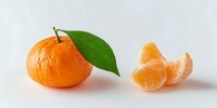 Fresh mandarin orange with green leaf next to peeled segments on white background, showcasing bright citrus fruit for food photography.