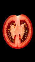 Fresh ripe tomato slice showing detailed internal structure with seeds and flesh on black background, dramatic lighting highlights natural texture and color.