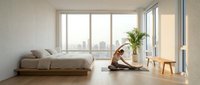 Young woman with medium skin tone in casual athletic wear practicing yoga stretching pose in minimalist bedroom with floor bed, wooden stool, potted plant, and floor-to-ceiling windows overlooking city skyline, wellness and home fitness concept.