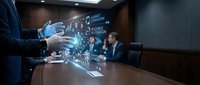 Businessman in blue suit gestures toward holographic digital interface displaying data analytics and network connections during corporate meeting in modern conference room.
