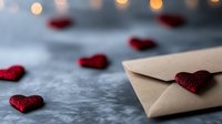 Romantic love letter with red glitter hearts scattered on gray surface and soft bokeh lights in background, Valentine's day concept for greeting cards.