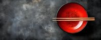 Empty red ceramic bowl with wooden chopsticks on dark concrete background with copy space. Traditional Asian dining setting for sushi and ramen.