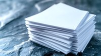 Stack of white blank paper sheets on wooden surface for office work and printing needs.