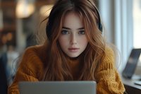Young Caucasian woman with long blonde hair wearing yellow sweater working on laptop computer in modern office environment for remote work concepts.